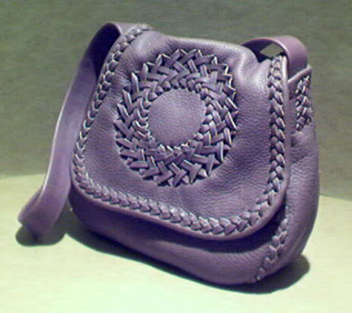  This handmade purse is made with 4 oz. moccasin cowhide leather. It is completely constructed with braiding using 1/4" wide laces out of that same leather. It has a long wide strap, a circle applique on the front, and a full width pocket on the inside/back of it. Leather, made in the USA, is the only material used for this purse. 