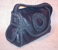  This Black braided leather purse has lots of pockets, a circle applique on it's flap, and a flat strap with braiding down the length of it. 