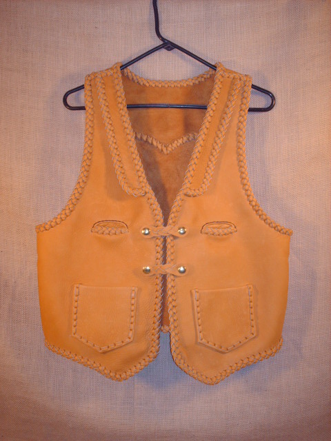  This moccasin cowhide leather vest was hand made in the USA using leather that was tanned in the USA. It features lapels, a pointed back yoke, two front slit breast pockets (credit card size), two patch hip pockets (without flaps), and two set of 'trick braid' snap closures. 