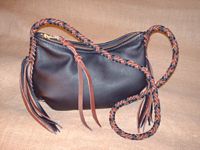  This medium size version of this style has a dark Brown body with two-toned braiding of its seams, strap (and its tassels). The large brass zipper has a leather strap attached to the slides tab. 