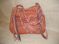  This Rust colored leather tote has two tone braiding (Rust and Mahogany). It has the two front pockets and the back inside pocket. It also has eight strand round braided straps with eight long tassels hanging from each end of them. 