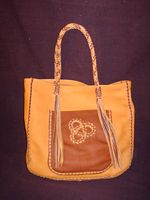  This front picture of this two tone tote shows the front pocket with the applique. It also shows the braided straps and the very long tassels that hang from each end of them. 