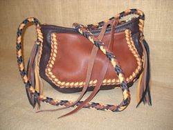  This small shoulder bag was made with four colors of leather. It's seams and strap are all braided. It's side pocket is also attached with braiding. It has a zipper across it's top that has a leather pull on the slider. 