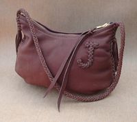  This small shoulder bag was made with Mahogany leather. It's seams are braided, as is it's 8 strand strap that has short tassels hanging from the ends. There is a capital 'J' braided on the side of it. 