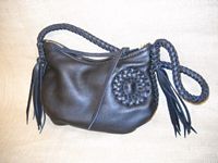  This Black bag has a braided circle applique on the side of it. 8 tassels hang from each end of the 8 lace braided strap. A leather lace is also attached to the zipper slide. 