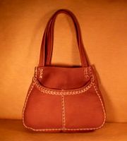  This small leather tote bag is about 13" wide (near the bottom) by 10" high by 3.5". It is completely made with full grain moccasin cowhide. 1/4" wide laces are used on the seams, across the front pockets, and to attach the straps. There are no other materials used on it. 