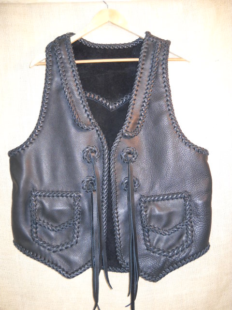 This custom, handmade moccasin cowhide leather vest was made in the USA using leather that was tanned in the USA. It features front lapels, a pointed back yoke, two patch hip pockets with flaps, and some straps that hang from some braided leather conchoes that I fashioned. 